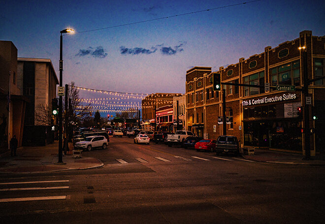 String lights glow above a downtown street, with cars parked down each side.
