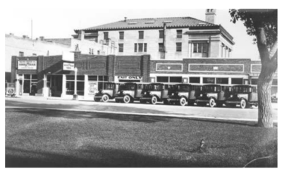 19TH-AND-PIONEER Vintage cars are parked in front of a row of buildings.