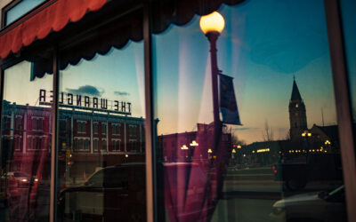 Window Reflection – 2 A reflection of Downtown Cheyenne, showcasing the Depot Clock Tower and exterior signage for The Wrangler.