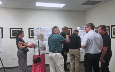 Plan of Development: BUSINESS-AND-PROPERTY-OWNER-MEETING A group of people gather around mounted presentations for the Plan of Development.