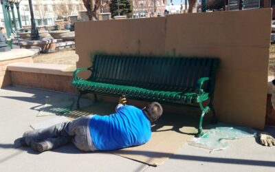 BENCH PAINT SPRAYING A man lays on the ground, spray painting a metal bench.