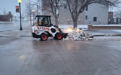 DOWNTOWN SNOW REMOVAL A bobcat machine shovels snow on a city street.