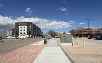 HEALTH WORKS ONEIL A sidewalk stretches between a parking lot and street, with a multi-story building in the background.