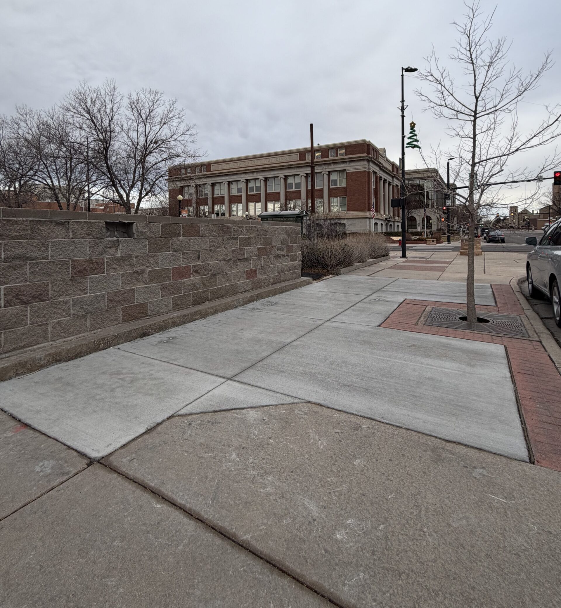 A sidewalk in Downtown Cheyenne, with a wall and tree.