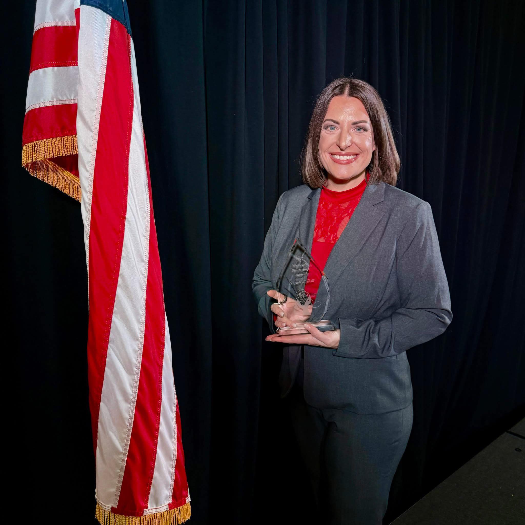 A smiling woman holds up an award alongside an American flag.